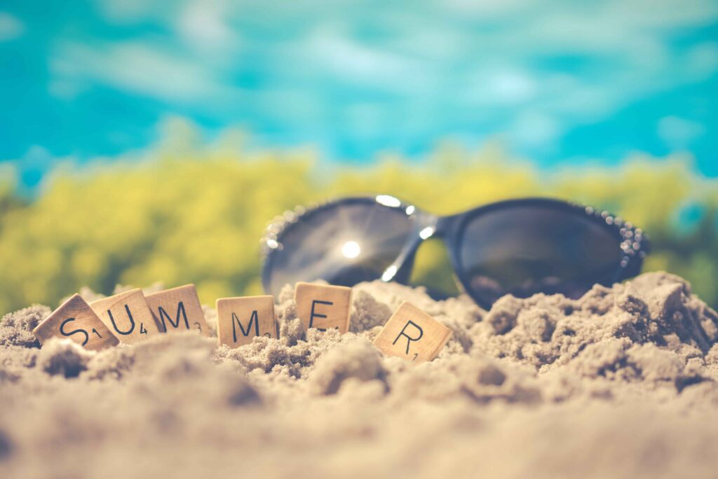 zonnebril in het zand met scrabble blokjes het woord summer